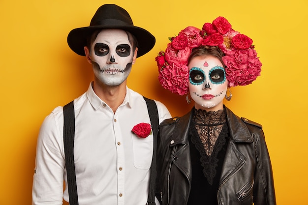 beängstigende Frau, Mann tragen kreatives Schädel-Make-up, schwarze Lederjacke, Hut, Pfingstrosenkranz, bereiten sich auf Halloween-Karneval oder Kostümparty vor