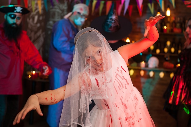 Beängstigendes kleines Mädchen auf einer Halloween-Party, verkleidet wie eine Braut im Jätkleid. Furchtsamer Pirat im Hintergrund.