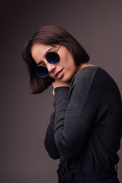 Beauty Fashion Brünette junges Modell Mädchen tragen stilvolle Sonnenbrille isoliert auf grau. Mode-Blogger