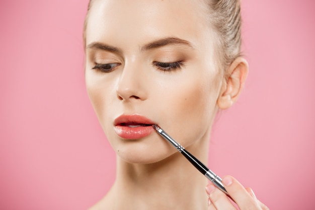 Beauty-Konzept - Frau mit roten Lippenstift mit rosa Studio Hintergrund. Schönes Mädchen macht Make-up.