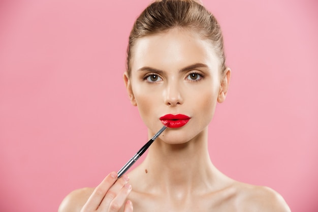 Beauty-Konzept - Frau mit roten Lippenstift mit rosa Studio Hintergrund. Schönes Mädchen macht Make-up.