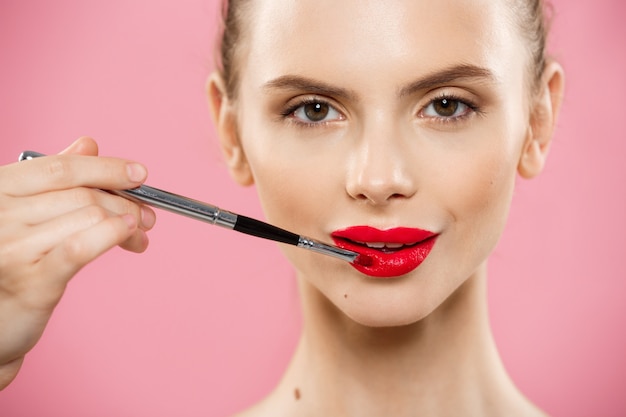 Beauty-Konzept - Frau mit roten Lippenstift mit rosa Studio Hintergrund. Schönes Mädchen macht Make-up.