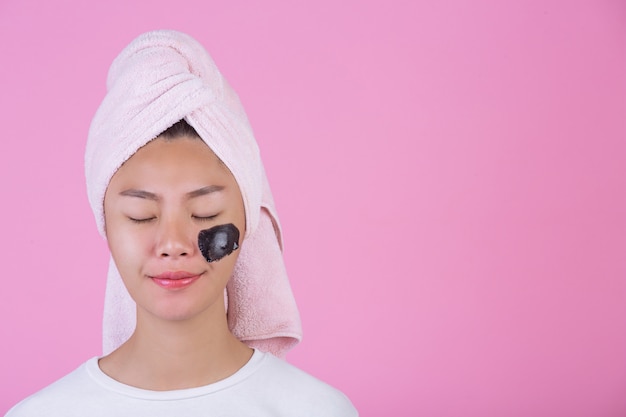 Beauty kosmetisches Peeling. Junge Frau mit Schwarzem ziehen weg Maske auf kosmetischem Hautpflege-Schalenprodukt der Haut auf Gesicht auf einem Rosa ab.