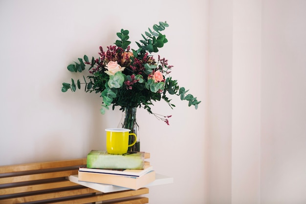 Becher auf Büchern nahe Blumenstrauß