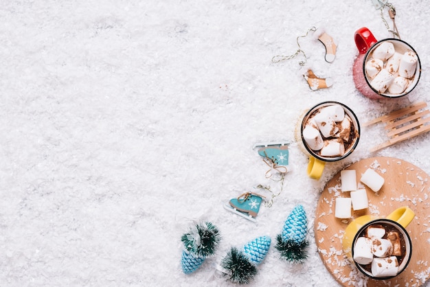 Becher mit Marshmallows und Getränken in der Nähe von Weihnachtsspielwaren auf Schnee
