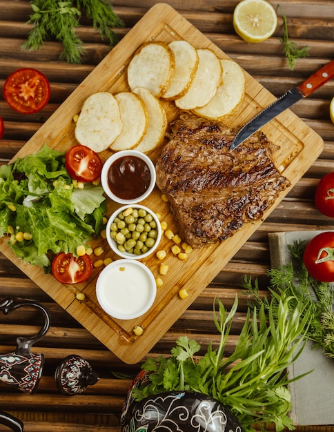 Beefsteak mit runden Bratkartoffeln auf einem Holztisch serviert mit grünem Salat, Bohnen und Mayonnaise