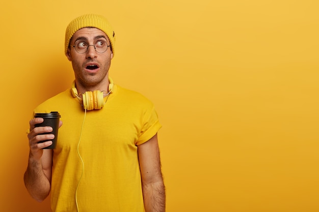 Beeindruckende junge steht sprachlos, trägt gelben Hut und lässiges T-Shirt