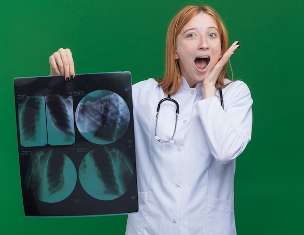 Kostenloses Foto beeindruckte junge ingwerärztin, die ein medizinisches gewand und ein stethoskop mit röntgenstrahlen trägt