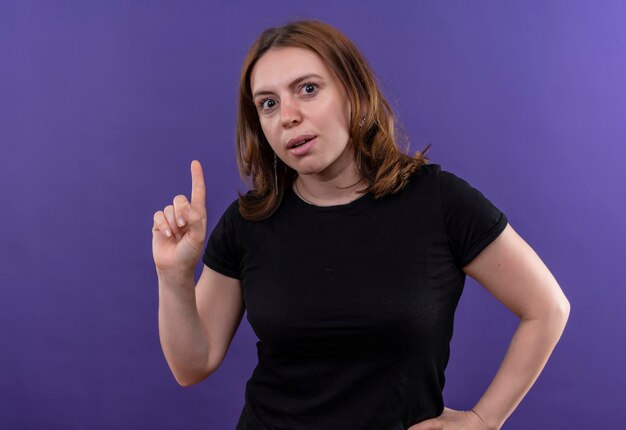 Beeindruckte junge lässige Frau mit erhobenem Finger und Hand auf Taille auf isoliertem lila Raum mit Kopienraum