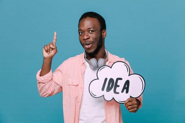 Beeindruckte Punkte halten Ideenblase junger afroamerikanischer Kerl mit Kopfhörern am Hals isoliert auf blauem Hintergrund