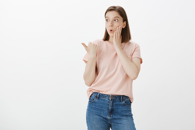 Beeindruckte und überraschte Frau, die Promo zeigt, nach links zeigt und erstaunt aussieht