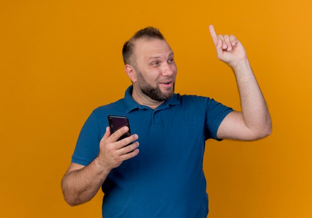 Beeindruckter erwachsener slawischer Mann, der Seite betrachtet, die Handy, das Finger hebt, hält