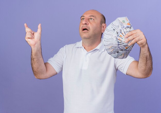 Beeindruckter lässiger reifer Geschäftsmann, der Geld hält, das Größe zeigt, die gerade lokalisiert auf lila Hintergrund schaut