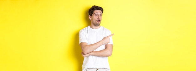 Beeindruckter Mann in weißem T-Shirt, der mit dem Finger nach links auf Promo zeigt, schauen Sie sich den Werbestan an