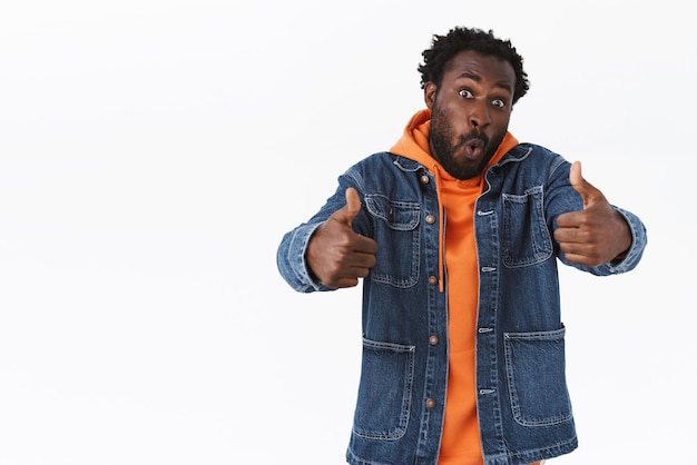 Beeindruckter und faszinierter gutaussehender afroamerikaner in jeansjacke, hoodie, daumen hoch in like und zustimmung