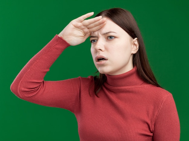 Beeindrucktes junges hübsches Mädchen, das die Hand auf der Stirn hält und seitlich in die Ferne schaut