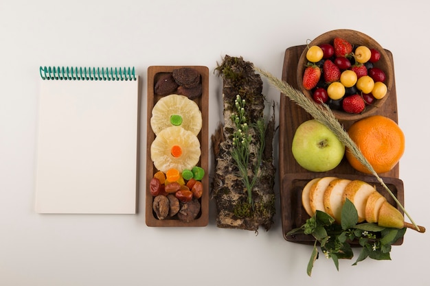 Beeren, Obstmischung und Kräuter auf einer Holzplatte mit einem Notizbuch beiseite