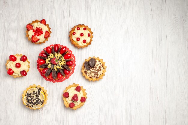 Beerenkuchen oben links auf dem roten ovalen Spitzendeckchen und verschiedene Törtchen auf dem weißen Holzboden