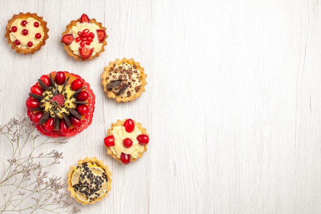 Beerenkuchen von oben links, umgeben von Beeren- und Schokoladentörtchen auf dem weißen Holzboden