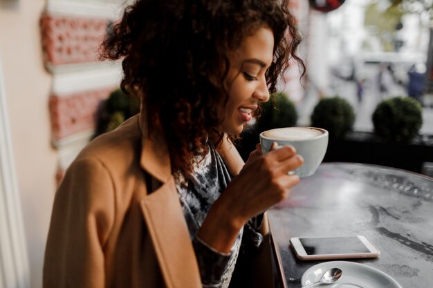 Begeisterte dunkelhäutige Hipster-Frau mit Afro-Frisur, die ihren Newsfeed überprüft