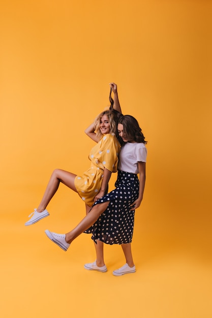 Begeisterte Freundinnen in trendigen Gummischuhen, die lustig auf Gelb tanzen. Wunderbare Schwestern, die Freizeit genießen.