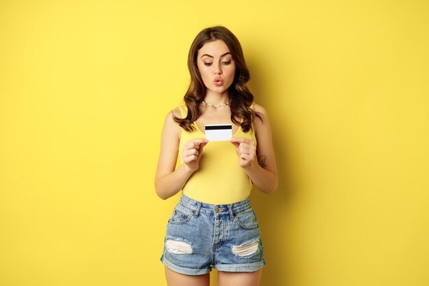 Begeisterte junge Frau, die Kreditkarte zeigt, Bank empfiehlt, Rabatt im Geschäft, kontaktlose Zahlung oder Cashback, über gelbem Hintergrund steht.