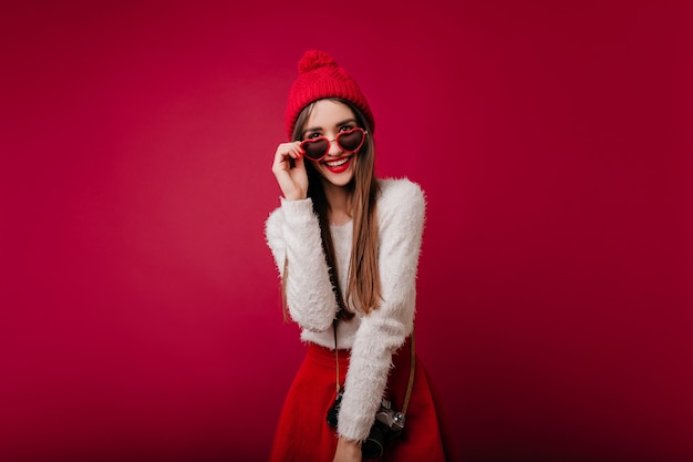 Begeisterte junge Frau mit trendigem Outfit, das ihre Brille berührt und lächelt