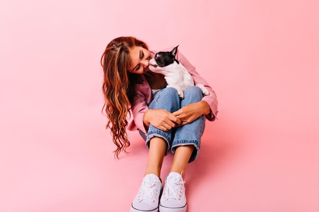 Begeistertes Mädchen, das ihren Welpen in der Nase küsst Studioporträt einer fröhlichen Dame, die die französische Bulldogge mit Liebe betrachtet