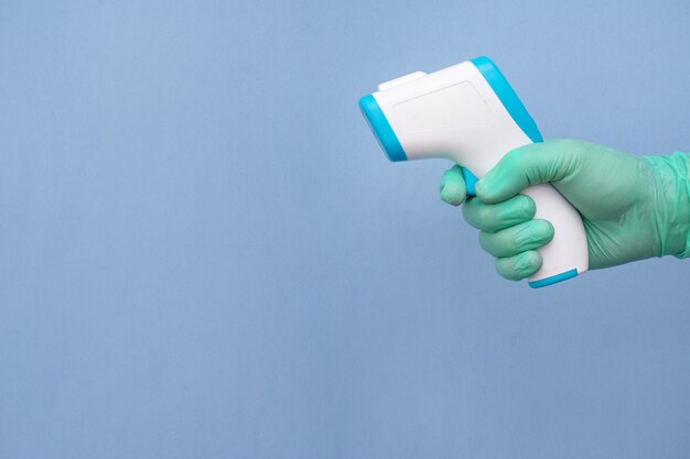 Behandschuhte Hand eines Gesundheitspersonals, das ein auf Blau isoliertes Thermometer hält