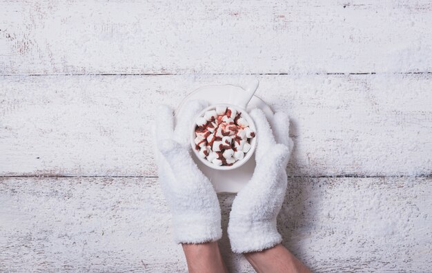 Behandschuhten Hände, die eine Tasse mit Marshmallows halten