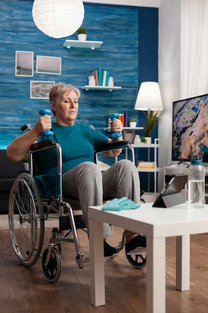 Behinderte ältere Frau, die Trainerhanteln hält, die Armübungen machen