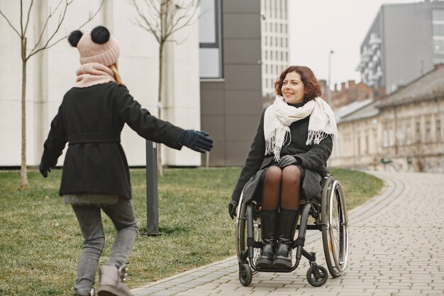 Behinderte Frau im Rollstuhl mit Tochter. Familie, die draußen im Park spazieren geht.