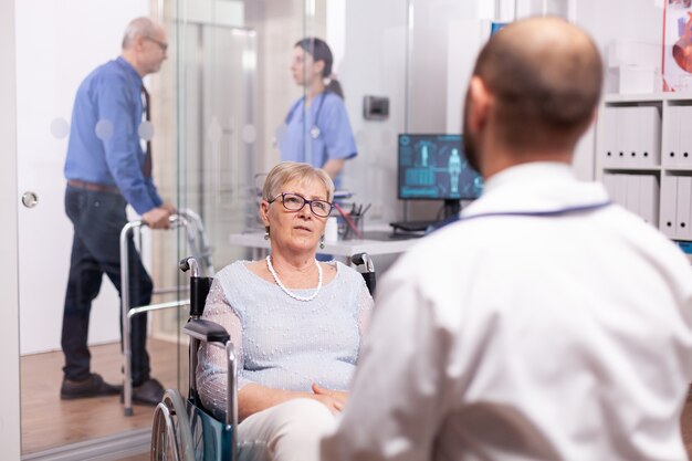 Behinderter älterer Patient im Rollstuhl im Gespräch mit Arzt im Krankenhaus