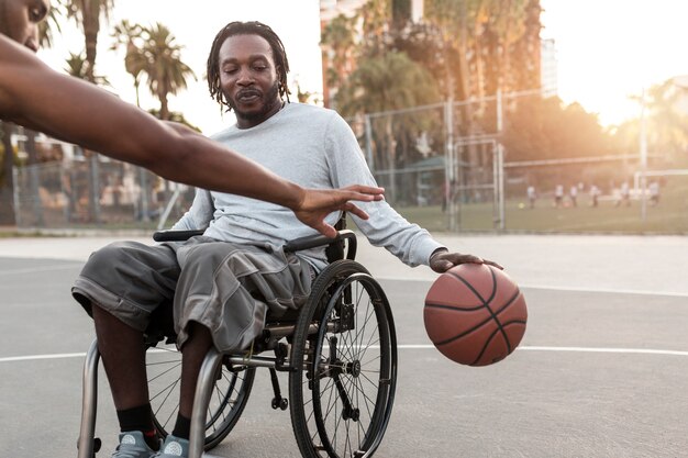Behinderter Mann im Rollstuhl, der mit seinen Freunden Basketball spielt