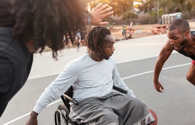 Behinderter Mann im Rollstuhl, der mit seinen Freunden Basketball spielt