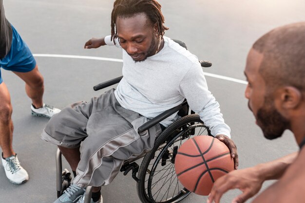 Behinderter Mann im Rollstuhl, der mit seinen Freunden Basketball spielt