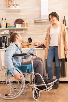 Behinderter mann im rollstuhl mit eierkarton für seine frau in der küche. behinderter, gelähmter, behinderter mann mit gehbehinderung, der sich nach einem unfall integriert.