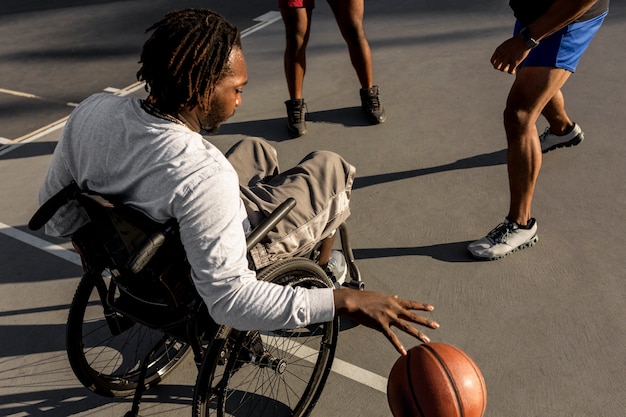 Behinderter Mann im Rollstuhl spielt Basketball mit seinen Freunden im Freien