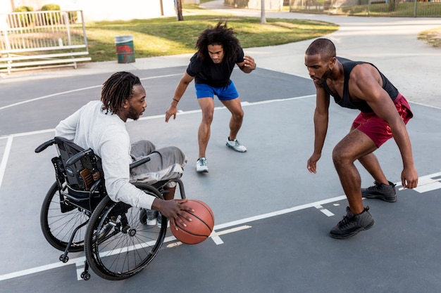Behinderter Mann im Rollstuhl spielt Basketball mit seinen Freunden im Freien