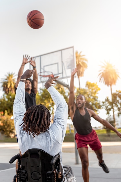 Behinderter Mann im Rollstuhl spielt Basketball mit seinen Freunden im Freien