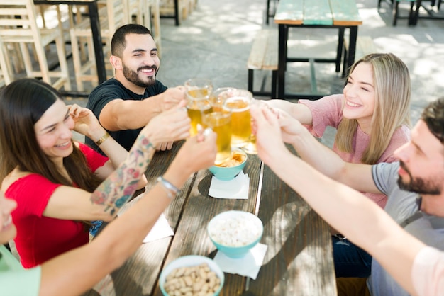 Kostenloses Foto beifall! fröhliche gruppe von freunden, die mit bier anstoßen. beste freunde genießen gemeinsam ein paar drinks in einer bar im freien und feiern