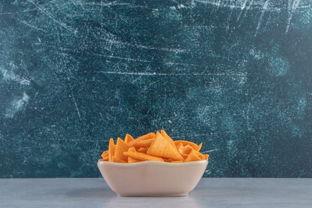 Beige Schüssel mit dreieckigen knusprigen Chips auf Steinhintergrund.