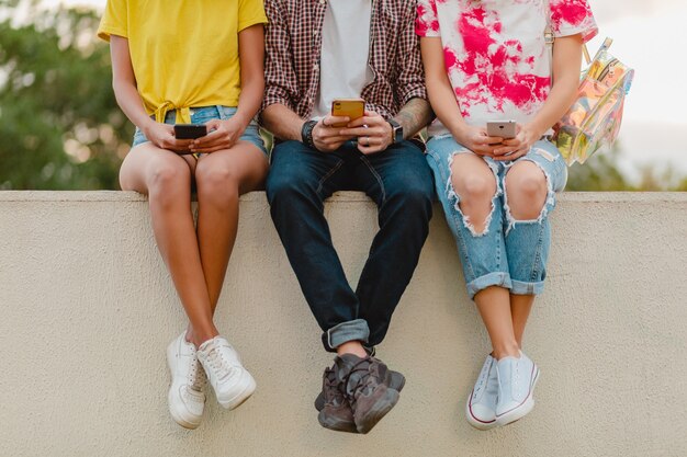 Beine in Turnschuhen der jungen Gesellschaft von Freunden, die Park mit Smartphones sitzen