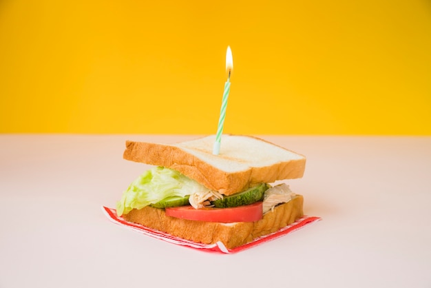 Beleuchtete Kerze über dem Sandwich auf weißem und gelbem Hintergrund