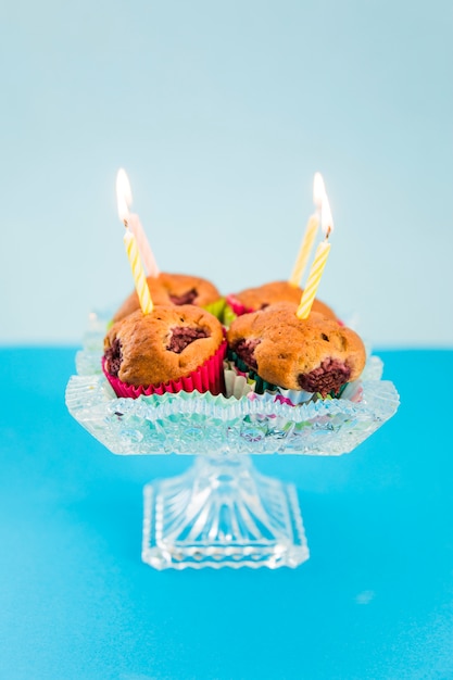 Beleuchtete Kerzen über dem kleinen Kuchen auf Kristallcakestand gegen blauen Hintergrund