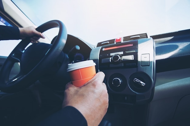 Bemannen Sie Antriebsauto beim Halten einer Schale heißen Kaffees - Autofahren schläfriges oder schlafendes Konzept