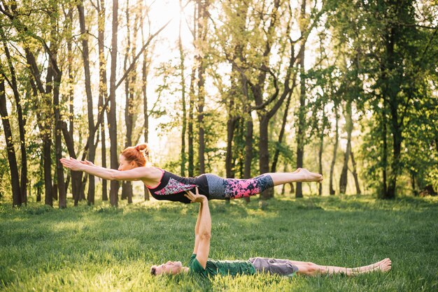 Bemannen Sie balancierende Frau auf seiner Hand beim Handeln von Yoga auf dem grasartigen Gebiet
