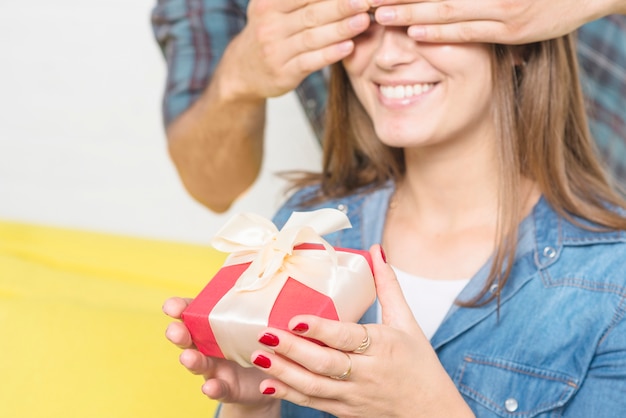 Bemannen Sie bedeckende Augen seiner glücklichen Freundin, die Valentinsgrußgeschenk hält