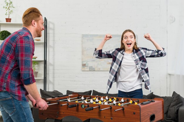 Bemannen Sie das Betrachten ihrer Freundin, die zujubelt, nachdem Sie den Tischfußball gewonnen haben