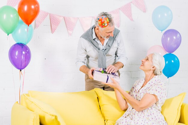 Bemannen Sie das Geben seiner Frau, die auf Sofa sitzt, Geburtstagsgeschenk